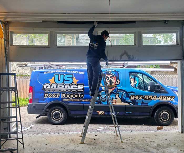 US Garage Door Repair technician standing on a ladder and fixing a broken garage door near Mount Prospect, IL